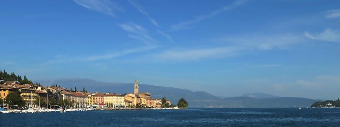 Trip Ayurveda beliebte Urlaubsziele am Gardasee -  Mit einer Fläche von 370 km² ist der Gardasee der größte See Italiens. Es liegt am Fuße der Alpen und erstreckt sich über drei Staaten: Lombardei, Venetien und Trentino. Die maximale Tiefe des Sees beträgt 346 m, er hat eine längliche Form und sein nördliches Ende ist sehr schmal. Dort ist der See von den Bergen der Gruppo di Baldo umgeben. Du trittst aus deinem gemütlichen Hotelzimmer und es begrüßt dich die warme italienische Sonne. Du blickst auf den atemberaubenden Gardasee, der in zahlreichen Blautönen schimmert - von tiefem Dunkelblau bis zu funkelndem Türkis. Majestätische Berge umgeben dich, während die Brise sanft deine Haut streichelt und der Duft von blühenden Zitronenbäumen deine Nase kitzelt. Du schlenderst die malerischen, engen Gassen entlang, vorbei an farbenfrohen, blumengeschmückten Häusern. Vereinzelt unterbricht das fröhliche Lachen der Einheimischen die friedvolle Stille. Du fühlst dich wie in einem Traum, der nicht enden will. Jeder Schritt führt dich zu neuen Entdeckungen und Abenteuern. Du probierst die köstliche italienische Küche mit ihren frischen Zutaten und verführerischen Aromen. Die Sonne geht langsam unter und taucht den Himmel in ein leuchtendes Orange-rot - ein spektakulärer Anblick.